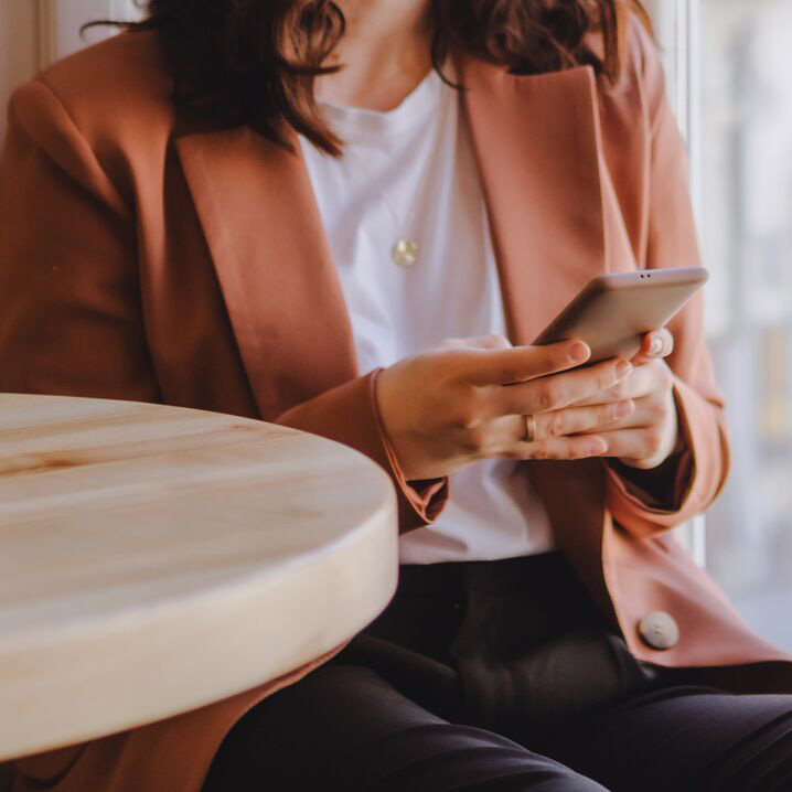 Sitting at table by window holding phone 900x900